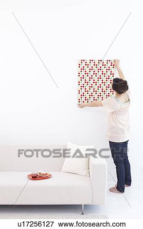 Stock Photo - Young woman hanging fabric on wall. Fotosearch