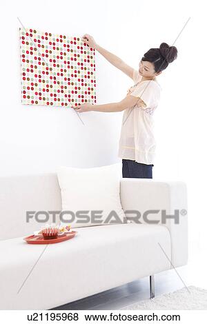 Stock Photo - Young woman hanging fabric on wall. Fotosearch