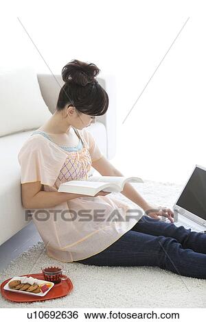Young woman holding a book and using laptop View Large Photo Image Stock Photograph - Young woman holding a book and using laptop. Fotosearch