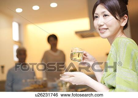 Stock Photograph - Young woman holding cup of herb tea, parents in background, differential focus. Fotosearch