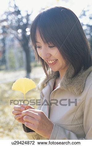 Stock Image - Young woman holding gingko leaf. Fotosearch