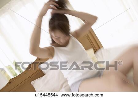 Picture - Young woman holding up hair on bed, blurred motion. Fotosearch