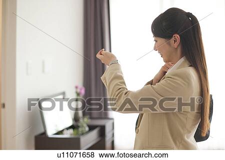 Stock Photo - Young woman looking at wristwatch, smiling. Fotosearch