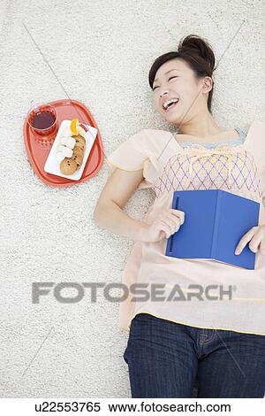 Stock Photography - Young woman lying on back holding a book. Fotosearch