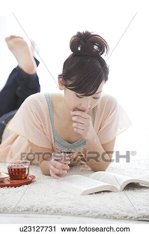 Stock Image - Young woman lying on front and reading a book. Fotosearch