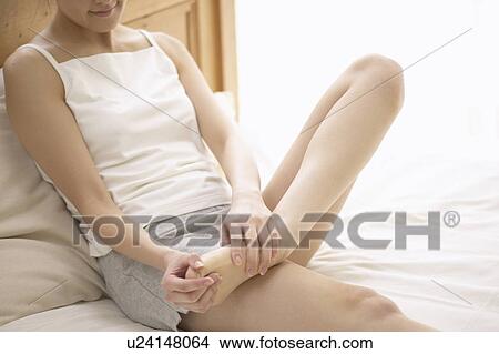 Picture - Young woman massaging foot on bed. Fotosearch
