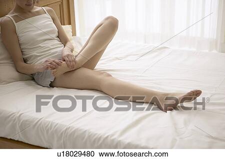 Stock Image - Young woman massaging foot on bed. Fotosearch