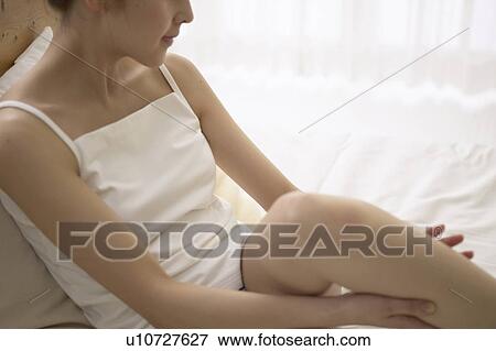 Stock Photo - Young woman massaging leg on bed. Fotosearch