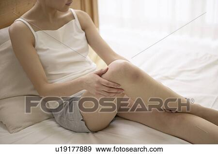 Stock Photo - Young woman massaging leg on bed. Fotosearch