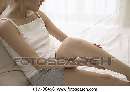 Stock Photograph - Young woman massaging leg on bed. Fotosearch