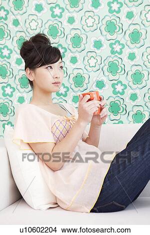 Young woman on a couch drinking coffee View Large Photo Image Picture - Young woman on a couch drinking coffee. Fotosearch
