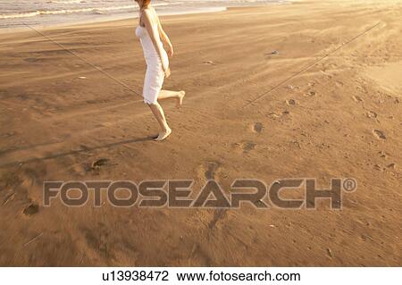 Stock Image - Young woman running on beach. Fotosearch