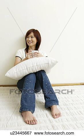 Stock Photo - Young woman sitting and holding cushion. Fotosearch