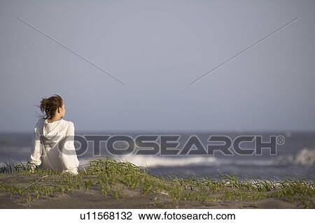 Stock Image - Young woman sitting on beach, copy space. Fotosearch