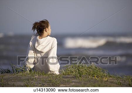 Stock Image - Young woman sitting on beach. Fotosearch