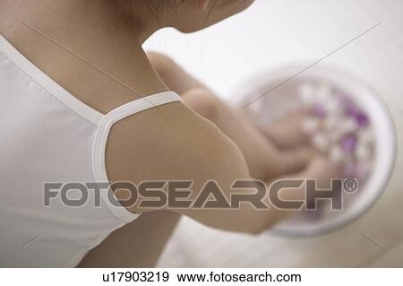 Stock Photo - Young woman soaking feet and hands in bowl of water with flower petals. Fotosearch