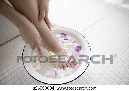 Picture - Young woman soaking foot in bowl of water with flower petals. Fotosearch