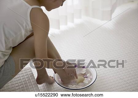 Young woman soaking foot in bowl of water with flower petals View Large Photo Image Stock Image - Young woman soaking foot in bowl of water with flower petals. Fotosearch