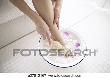 Stock Photo - Young woman soaking foot in bowl of water with flower petals. Fotosearch