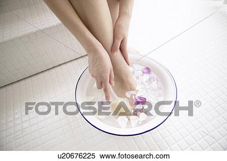 Stock Photography - Young woman soaking foot in bowl of water with flower petals. Fotosearch
