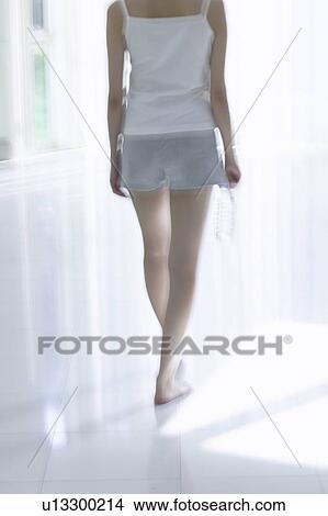 Picture - Young woman standing by window, holding bottle of water. Fotosearch
