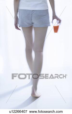 Stock Photo - Young woman standing by window, holding glass of juice, soft focus. Fotosearch