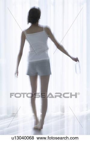 Young woman standing by window, holding bottle of water, soft focus, blurred motion View Large Photo Image Stock Photo - Young woman standing by window, holding bottle of water, soft focus, blurred motion. Fotosearch