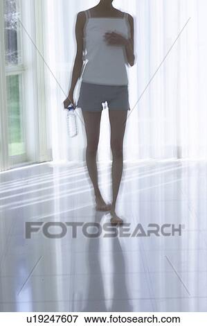Stock Photo - Young woman standing by window, holding bottle of water, soft focus, blurred motion. Fotosearch