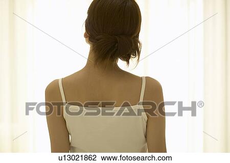 Stock Image - Young woman standing by window. Fotosearch