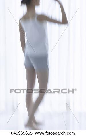 Stock Photography - Young woman standing by window, drinking bottle of water, soft focus, blurred motion. Fotosearch