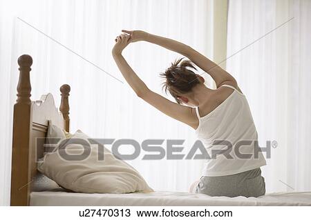Stock Image - Young woman stretching on bed. Fotosearch