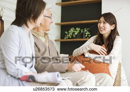 Stock Image - Young woman talking to her parents on sofa. Fotosearch
