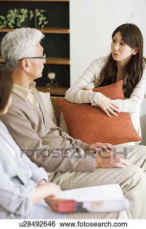 Stock Photograph - Young woman talking to her parents on sofa. Fotosearch