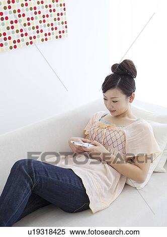 Stock Photography - Young woman text messaging on a couch. Fotosearch