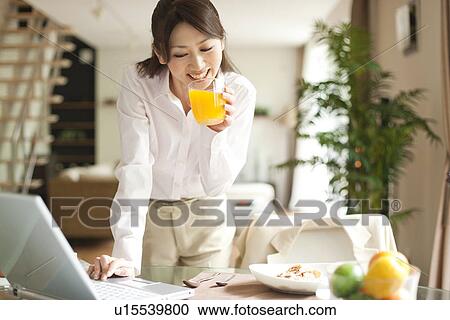 Young woman using laptop at table, holding glass of orange juice View Large Photo Image Stock Image - Young woman using laptop at table, holding glass of orange juice. Fotosearch