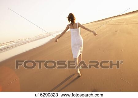 Stock Image - Young woman walking on beach. Fotosearch