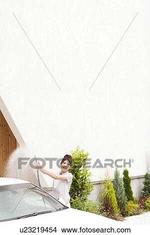 Young woman washing car, holding hose, copy space View Large Photo Image Picture - Young woman washing car, holding hose, copy space. Fotosearch