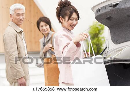 Stock Photo - Young woman with parents picking shopping bag from boot. Fotosearch