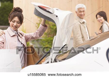 Stock Photography - Young woman with parents picking shopping bag from boot. Fotosearch