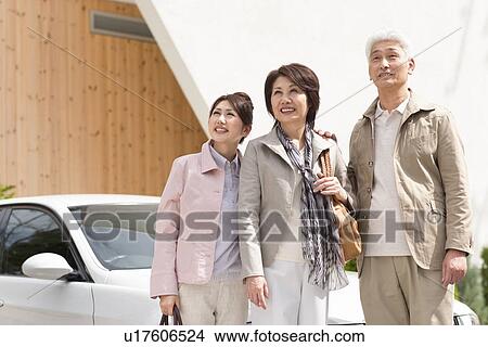 Picture - Young woman with parents standing by car, smiling and looking away. Fotosearch