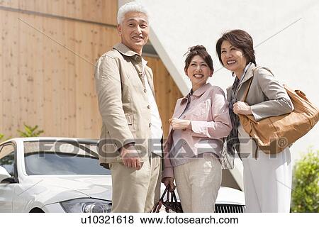 Stock Photo - Young woman with parents standing by car, smiling and looking away. Fotosearch