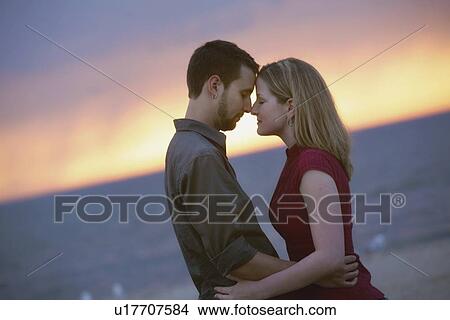a couple standing by the water at sunset View Large Photo Image Picture - a couple standing by the water at sunset. Fotosearch