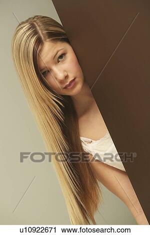 Stock Image - a girl in a white dress hiding behind a wall. Fotosearch