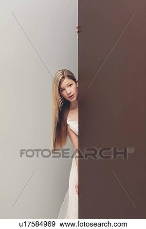 Stock Photo - a girl in a white dress looking around the corner. Fotosearch