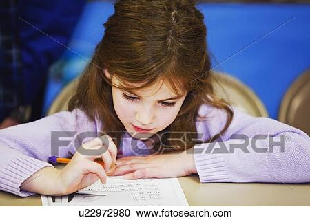 Stock Image - a girl sitting at a table and doing work with a pencil and paper. Fotosearch