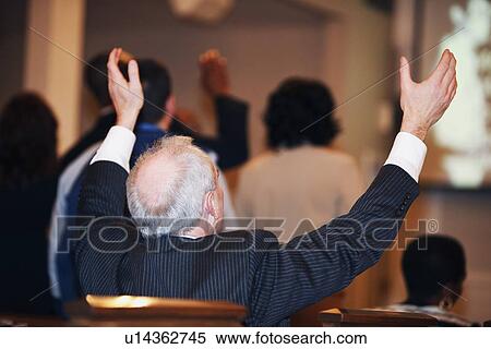 Stock Photography - a man sitting in church with hands raised. Fotosearch