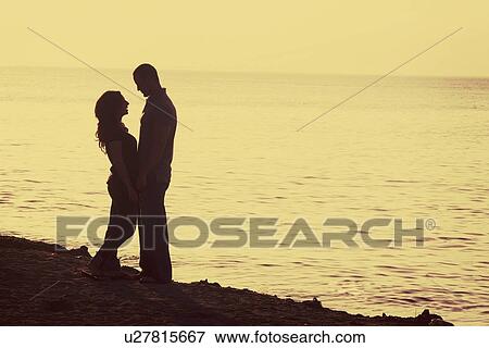 Stock Photo - silhouette of a couple standing on the beach. Fotosearch