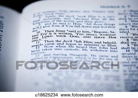 Picture - the bible open to matthew 4: 10 where jesus is tempted in the wilderness. Fotosearch