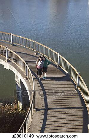 Stock Photo - two teenage girls on a pedestrian bridge over a river. Fotosearch