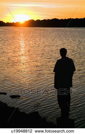 Stock Image - willmar, minnesota, united states of america; silhouette of a man standing on the shore watching the sunset. Fotosearch